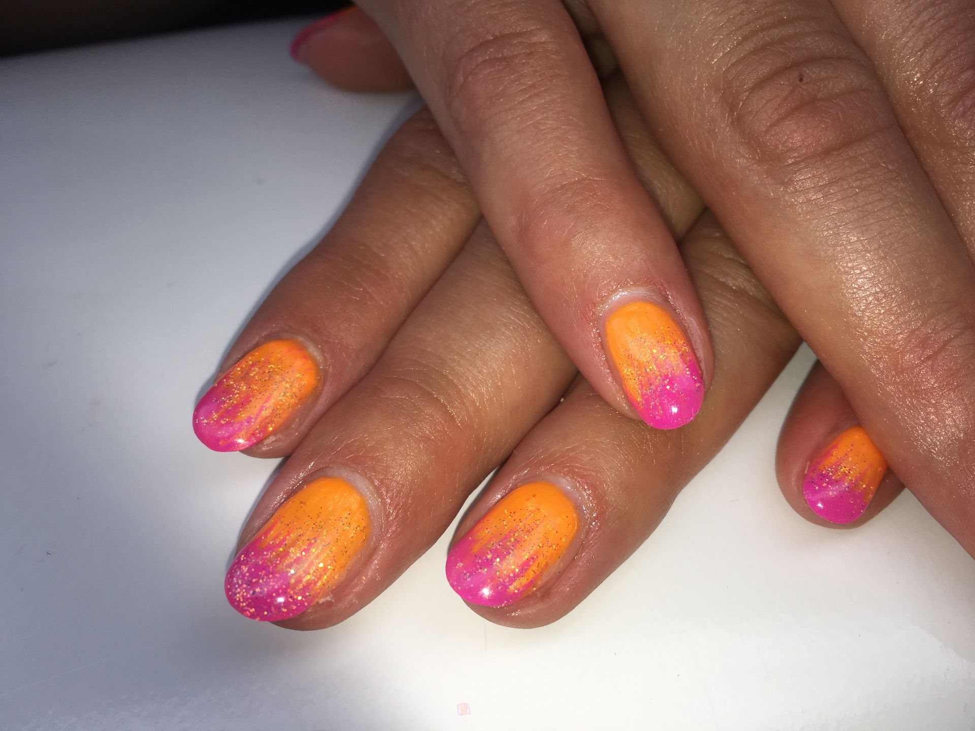 Orange-Pink Ombre Maniküre mit feinem Glitzer auf mandelförmigen Nägeln mit glänzendem Gel-Finish.