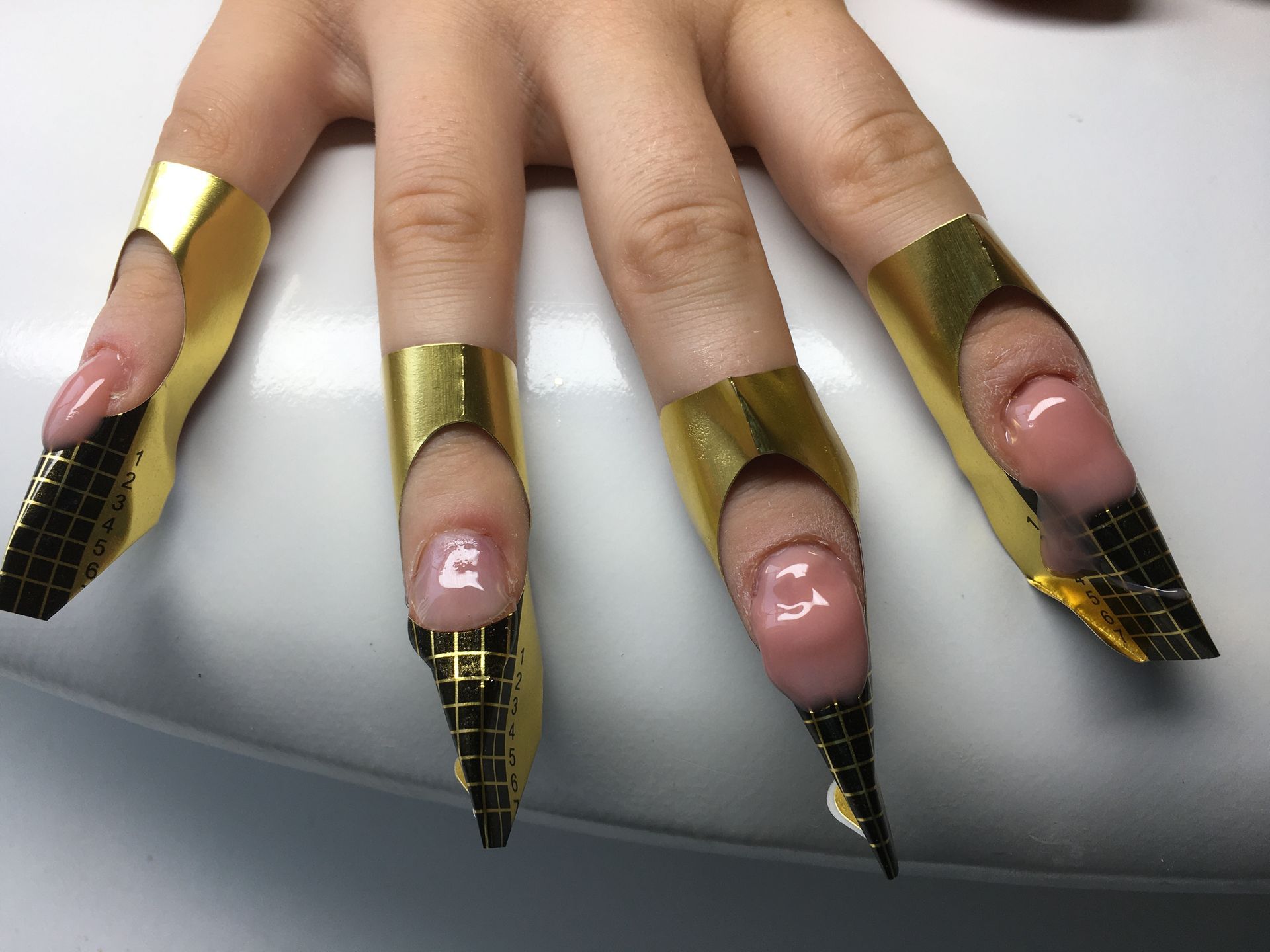 Nagelverlängerung mit goldenen Schablonen während der Modellage für lange, spitze Kunstnägel.