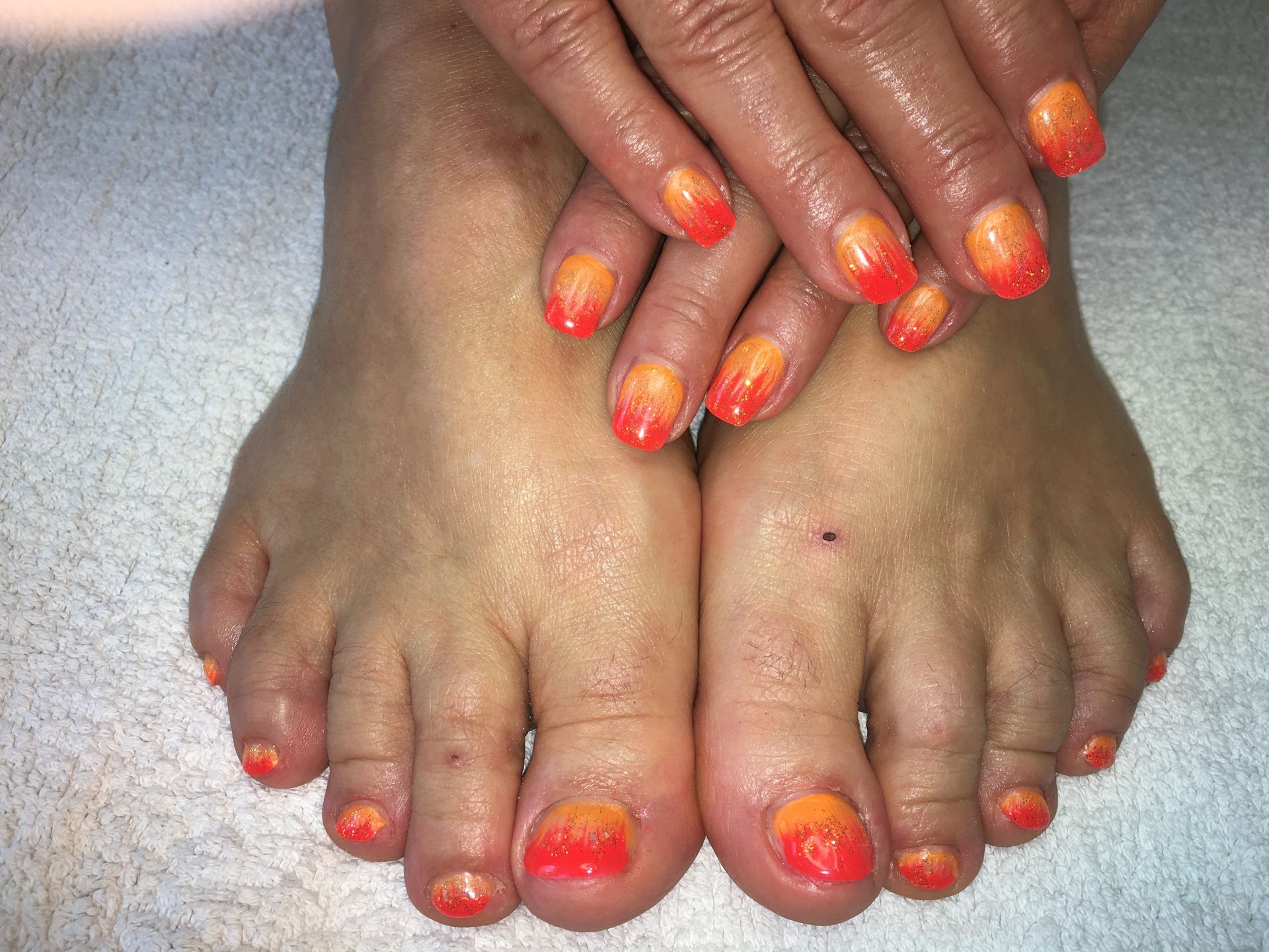 Sommerliche Pediküre und Maniküre mit Orange-Pink Ombre und Glitzer auf Finger- und Fußnägeln.