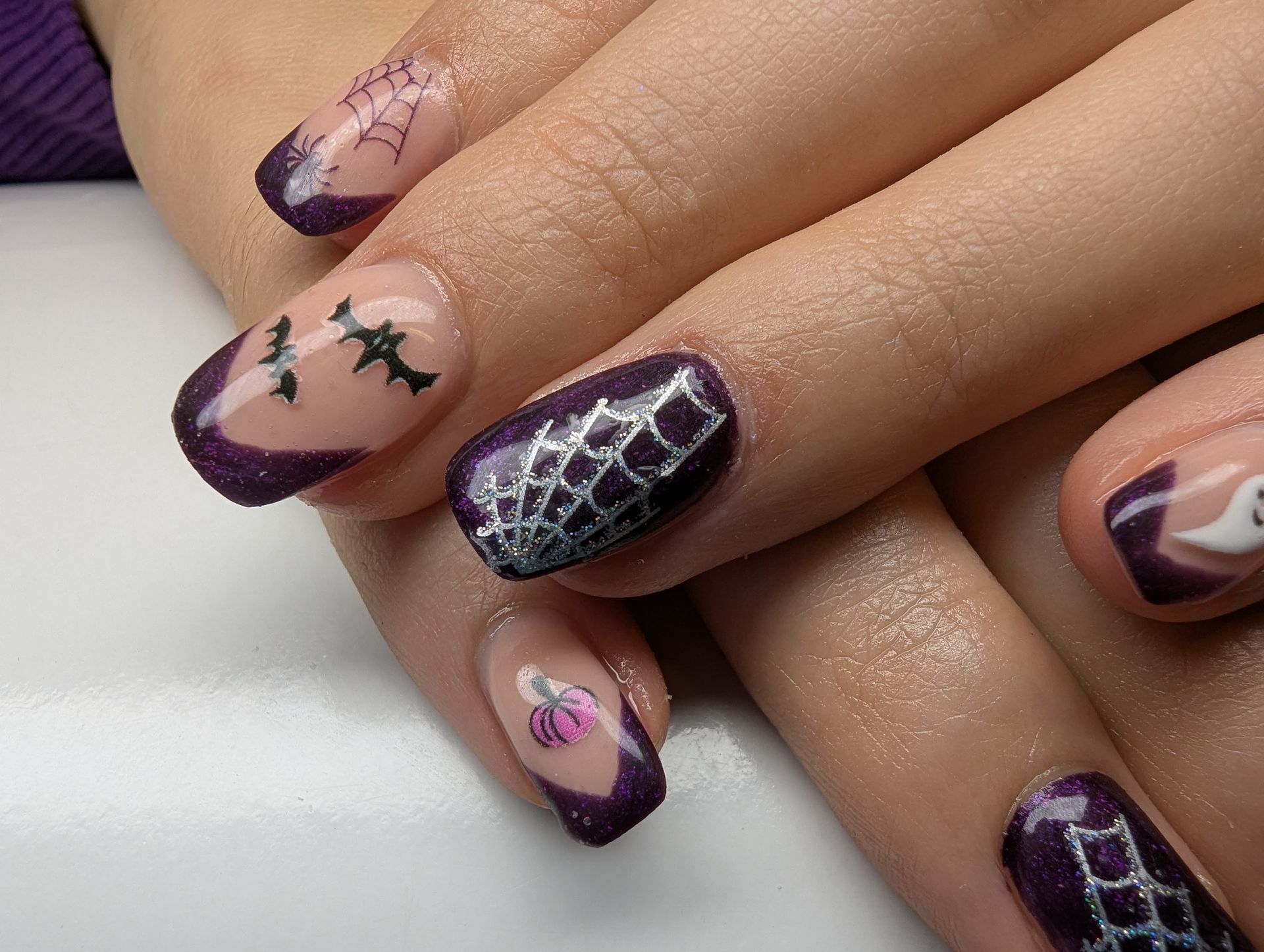 Dunkellila Glitzer Maniküre mit Halloween-Nailart wie Spinnennetz und Fledermäusen auf kurzen Nägeln.