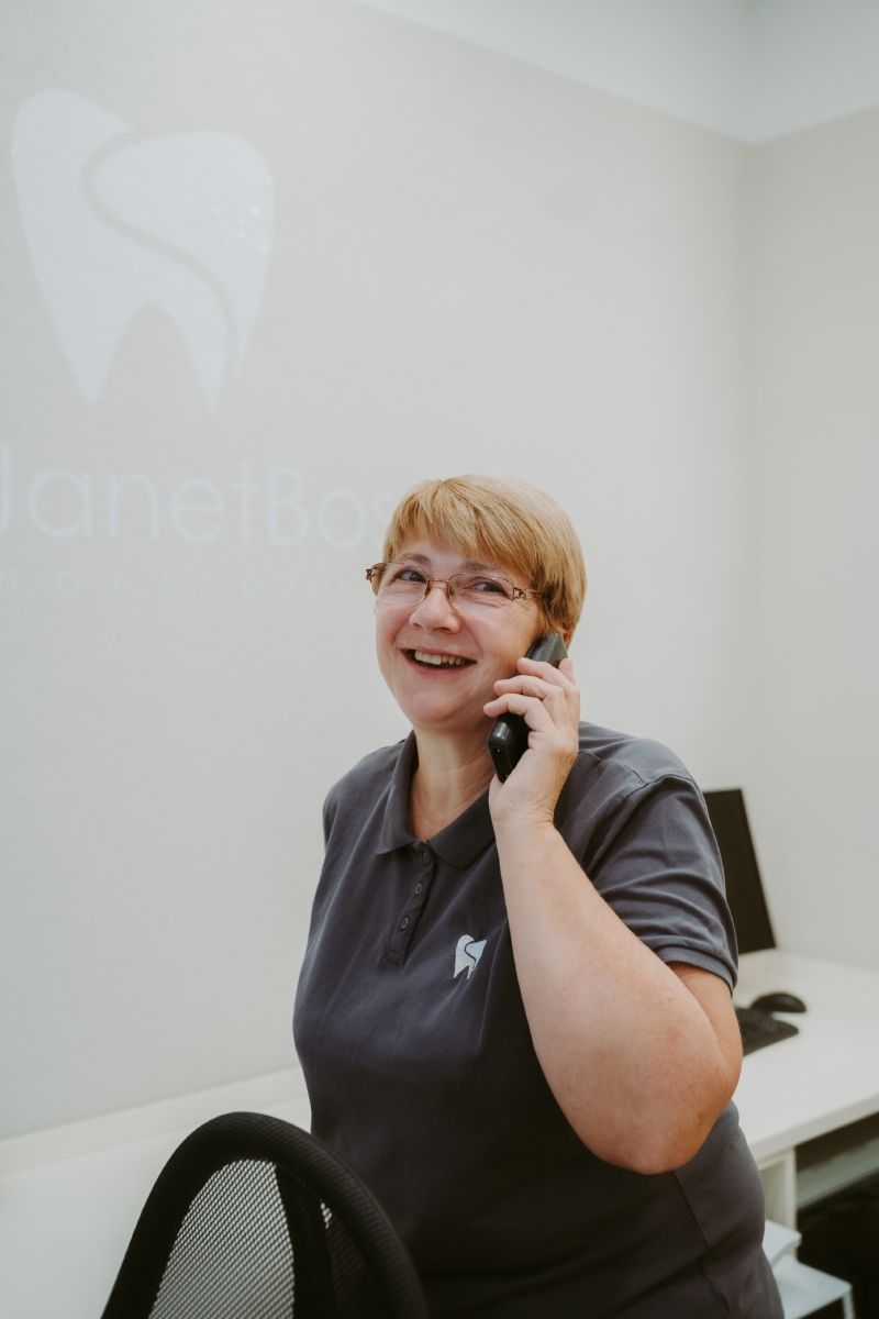 Eine Frau in einem grauen Poloshirt lächelt, während sie in einer Zahnarztpraxis telefoniert.