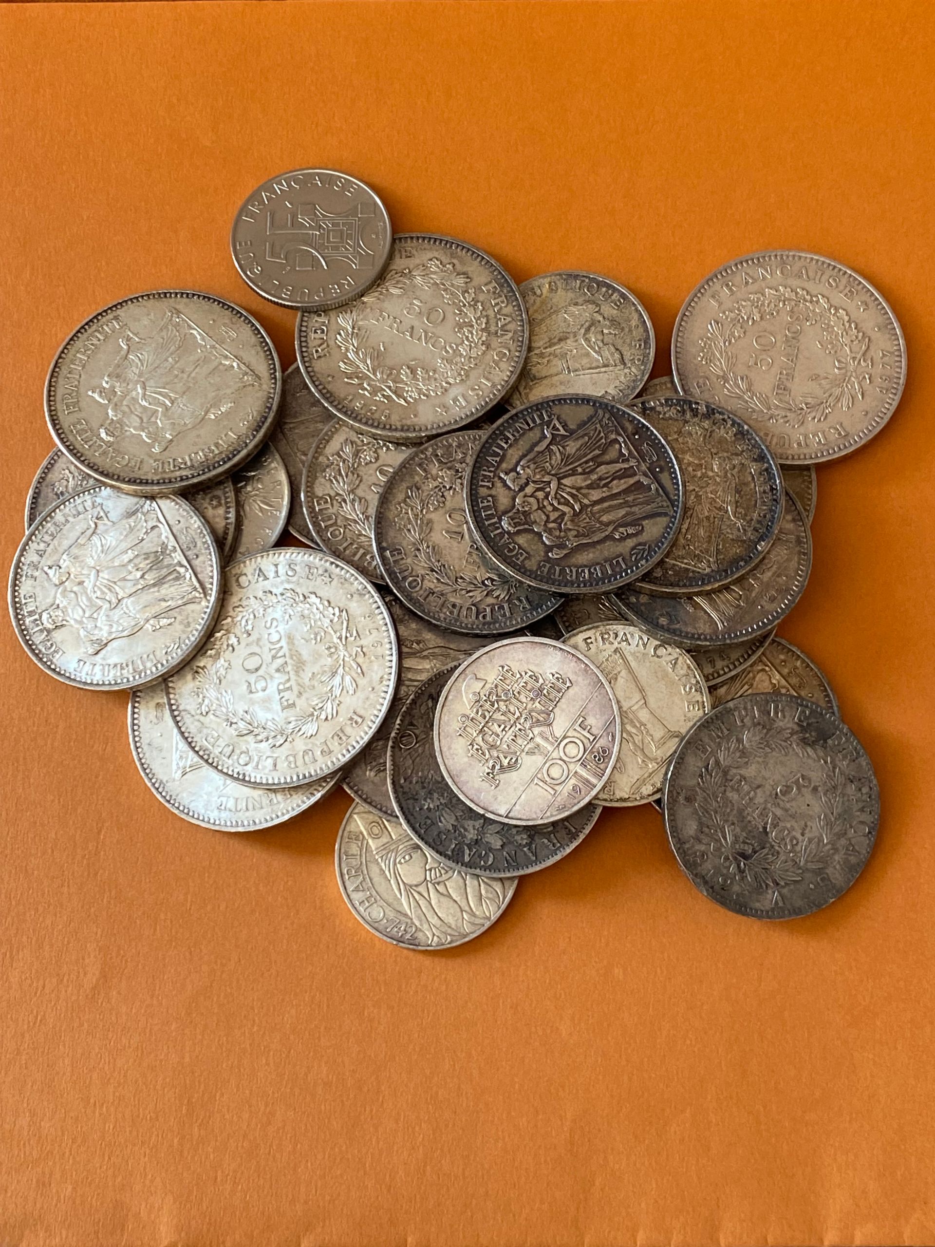 Pile de pièces d'argent sur une surface orange ; différentes tailles et états, certaines foncées avec l'âge.