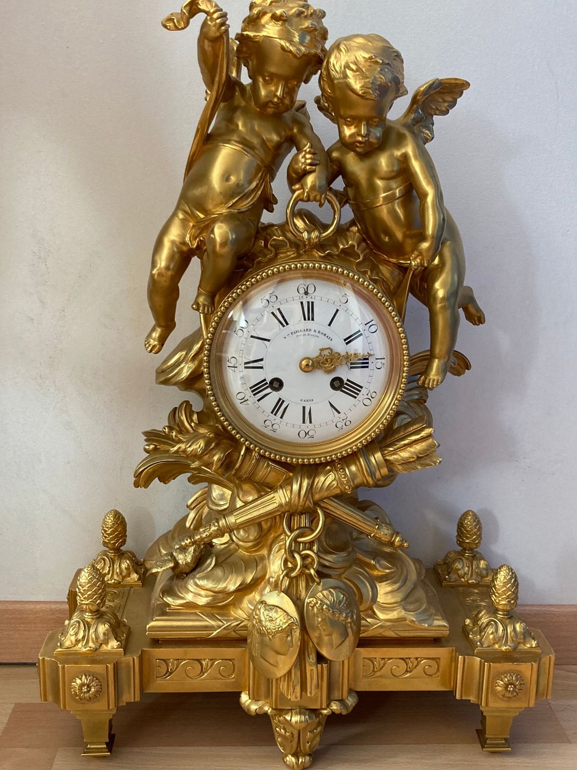 Horloge en or avec deux chérubins, cadran détaillé et base décorative.