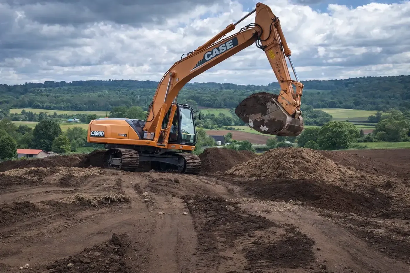 Excavadora Orange Case moviendo tierra en un sitio de construcción con colinas verdes en el fondo.