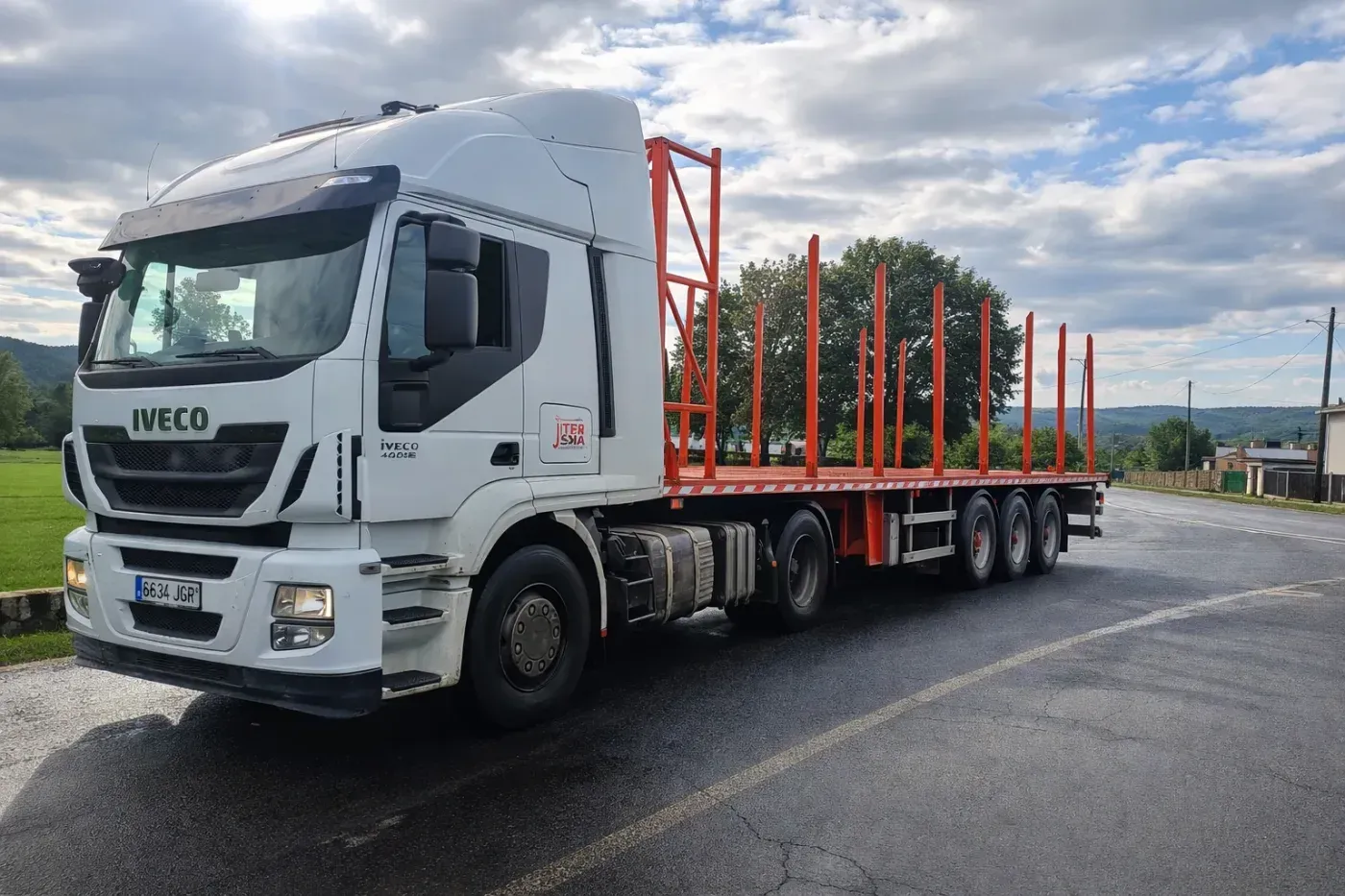 Camión semirremolque blanco con plataforma vacía en una carretera con curvas. Barandillas rojas. Cielo nublado.