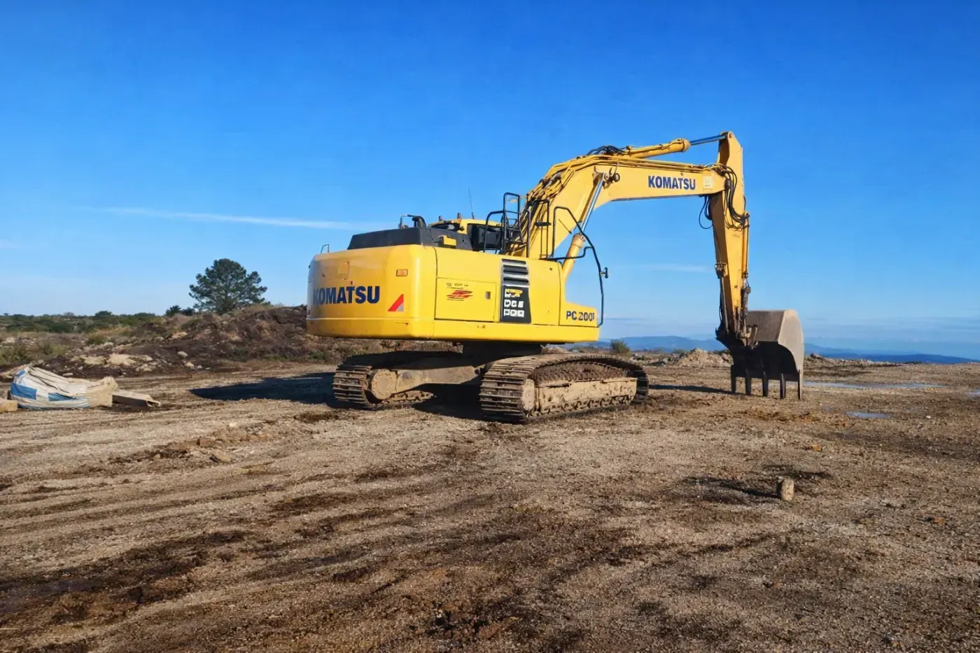 Excavadora Komatsu amarilla en un sitio de construcción bajo un cielo azul claro.
