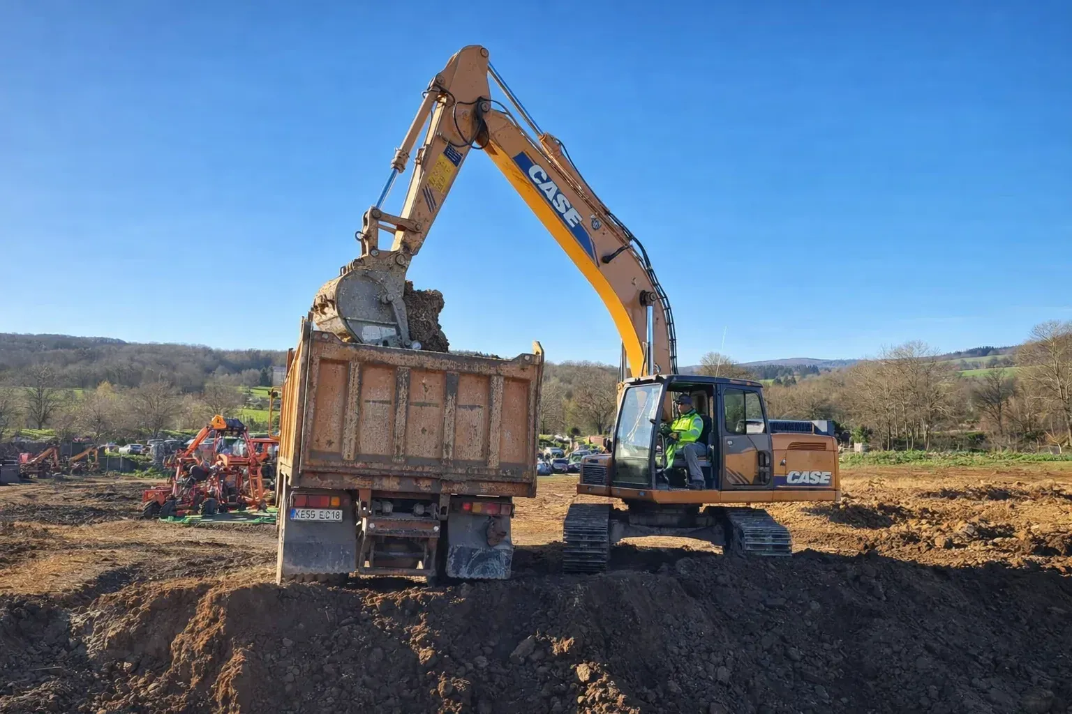 Excavadora cargando un camión volquete con tierra en un sitio de construcción en un día soleado.