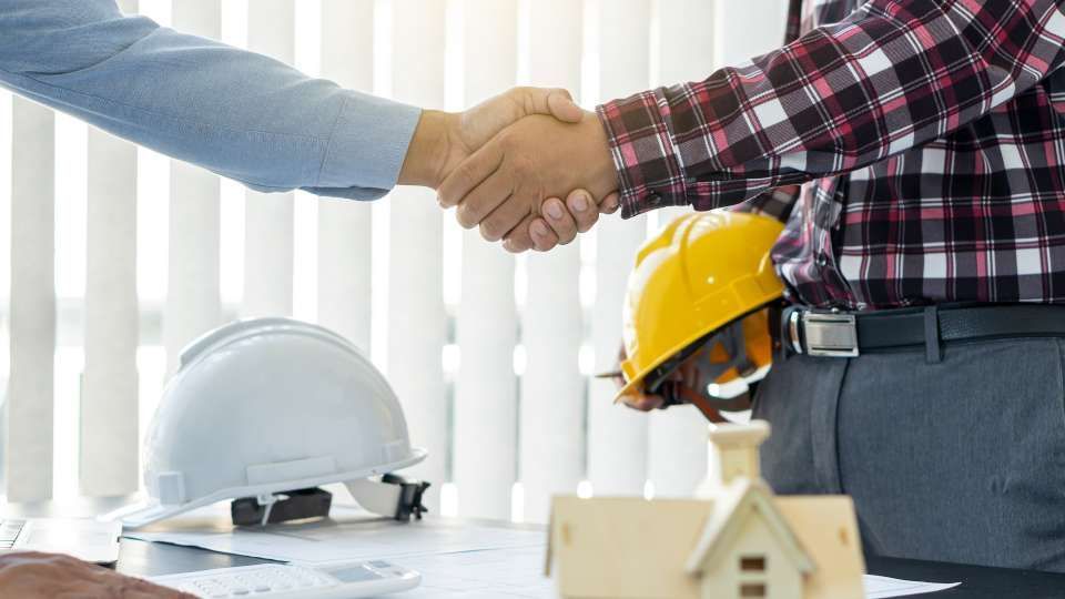 Ein Mann und eine Frau geben sich vor einem Musterhaus die Hand.