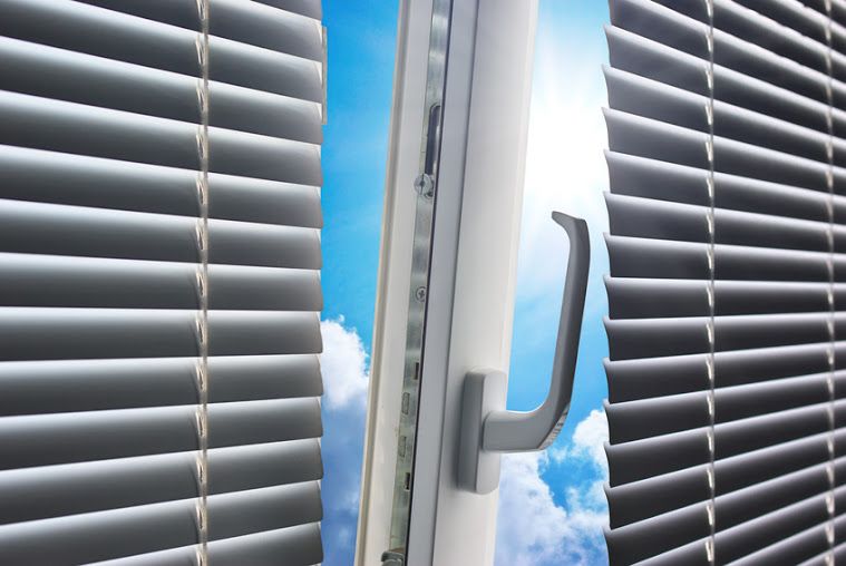 Fenêtre ouverte avec stores, ciel bleu visible, soleil qui filtre à travers.