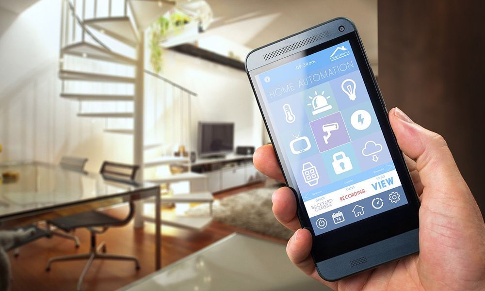 Une main tenant un smartphone affichant un panneau de commande domotique sur fond d'intérieur flou.