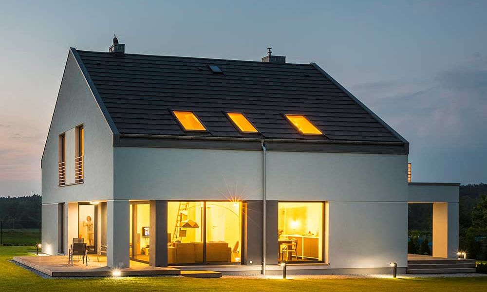 Maison blanche moderne au crépuscule, intérieur éclairé, pelouse et ciel.