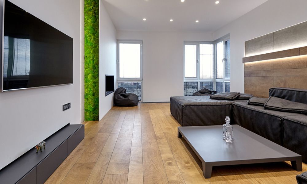 Salon moderne avec télévision, canapé d'angle noir et parquet. Mur végétal vertical.