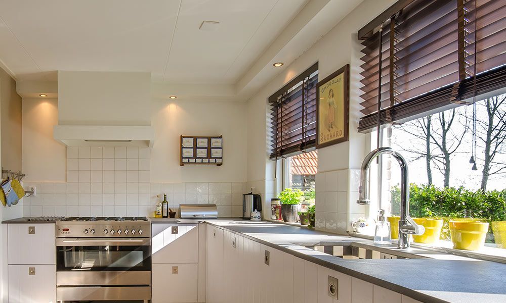 Cuisine lumineuse et blanche avec une cuisinière en acier inoxydable, un évier et des stores en bois foncé.