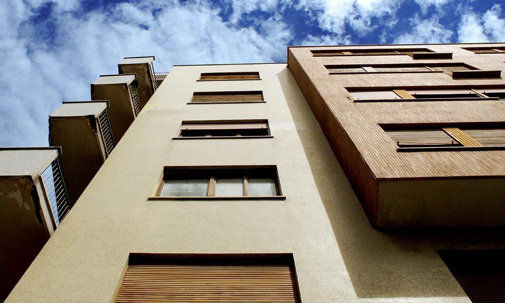Vue en contre-plongée d'un bâtiment moderne aux façades beiges et brunes se détachant sur un ciel bleu nuageux.