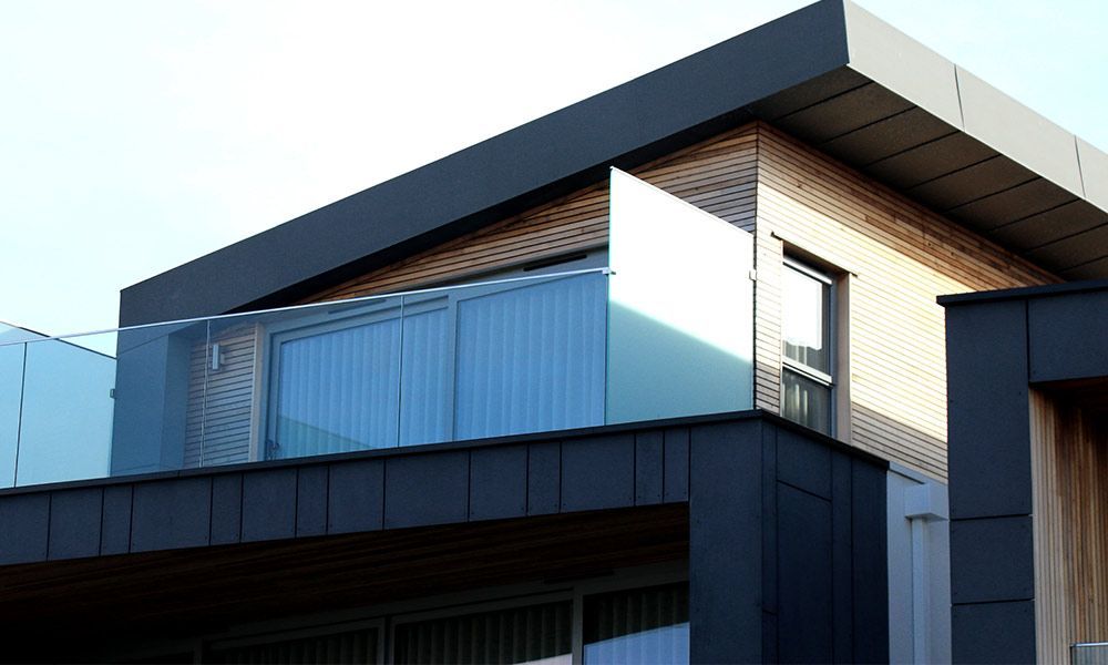Façade moderne du bâtiment avec balcon vitré, panneaux sombres et bardage en bois clair.