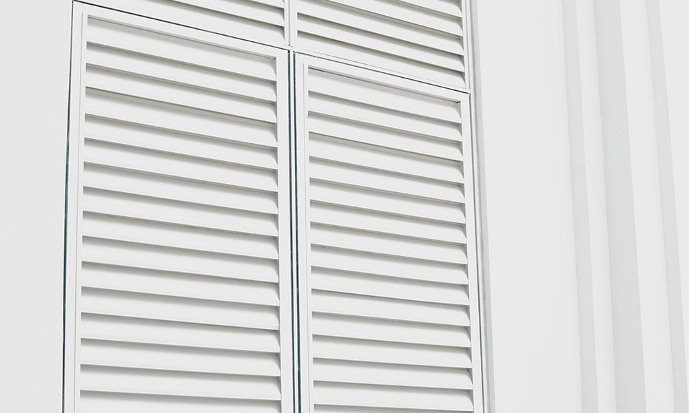 Volets blancs à persiennes sur la façade blanche d'un bâtiment.