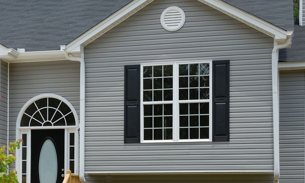 Extérieur de maison grise avec fenêtre, volets et porte cintrée.