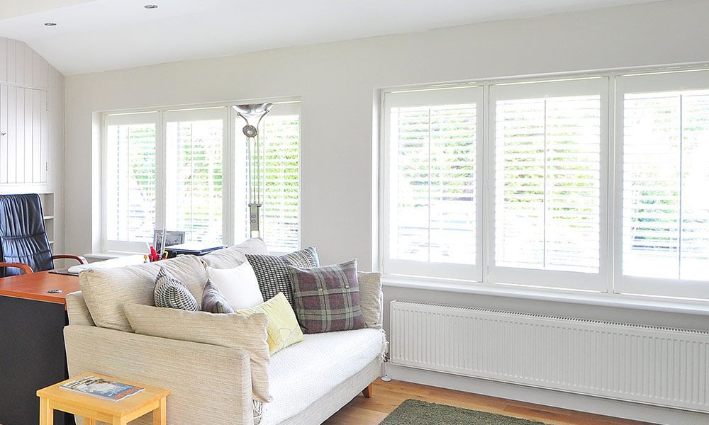 Salon avec volets blancs, canapé et radiateur sous les fenêtres.