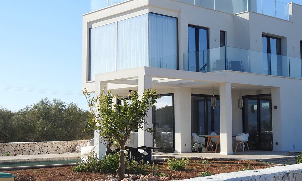 Immeuble blanc moderne avec balcons vitrés et grandes fenêtres par une journée ensoleillée.