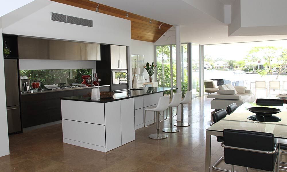 Cuisine moderne ouverte avec meubles blancs et îlot central, donnant sur une terrasse extérieure et une vue sur l'eau.