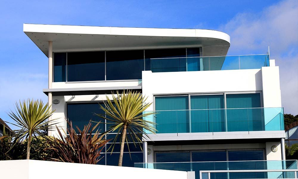 Maison moderne blanche avec de grandes fenêtres teintées bleutées et des balcons vitrés.