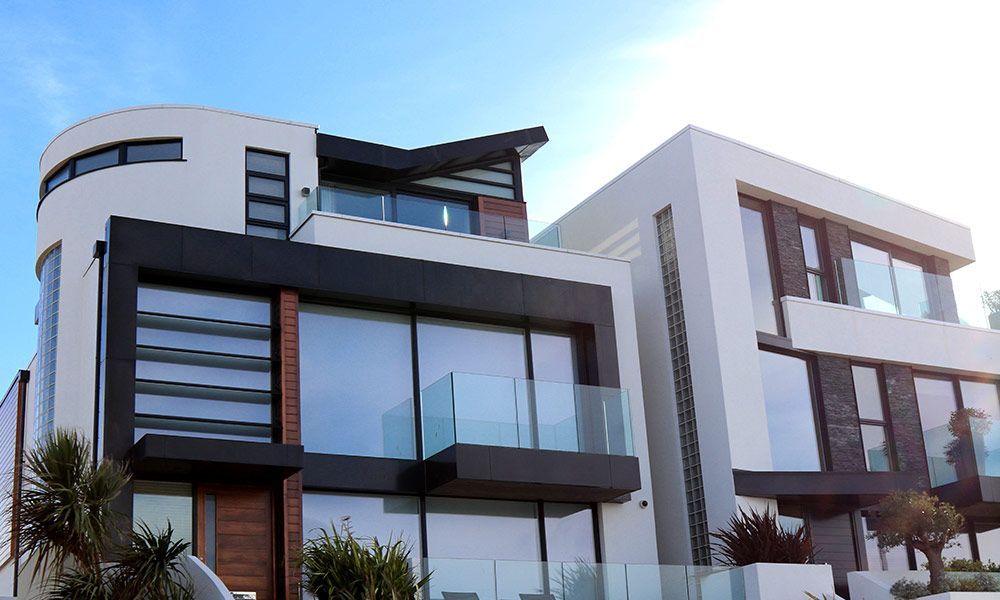 Maison moderne à plusieurs étages, blanche et noire, avec balcons vitrés et grandes fenêtres.