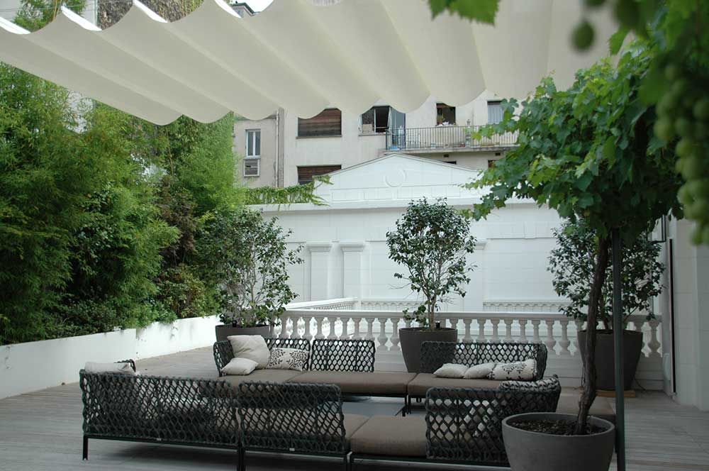 Terrasse extérieure avec mobilier en osier, plantes en pot et auvent blanc.