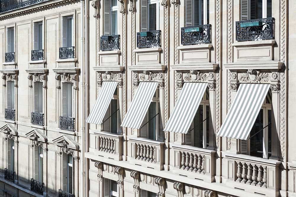 Élégante façade en pierre avec des auvents rayés protégeant les fenêtres du soleil.