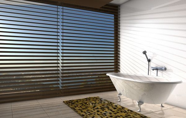 Baignoire sur pieds dans une salle de bains avec une grande fenêtre recouverte de stores horizontaux, tapis à motifs jaunes.