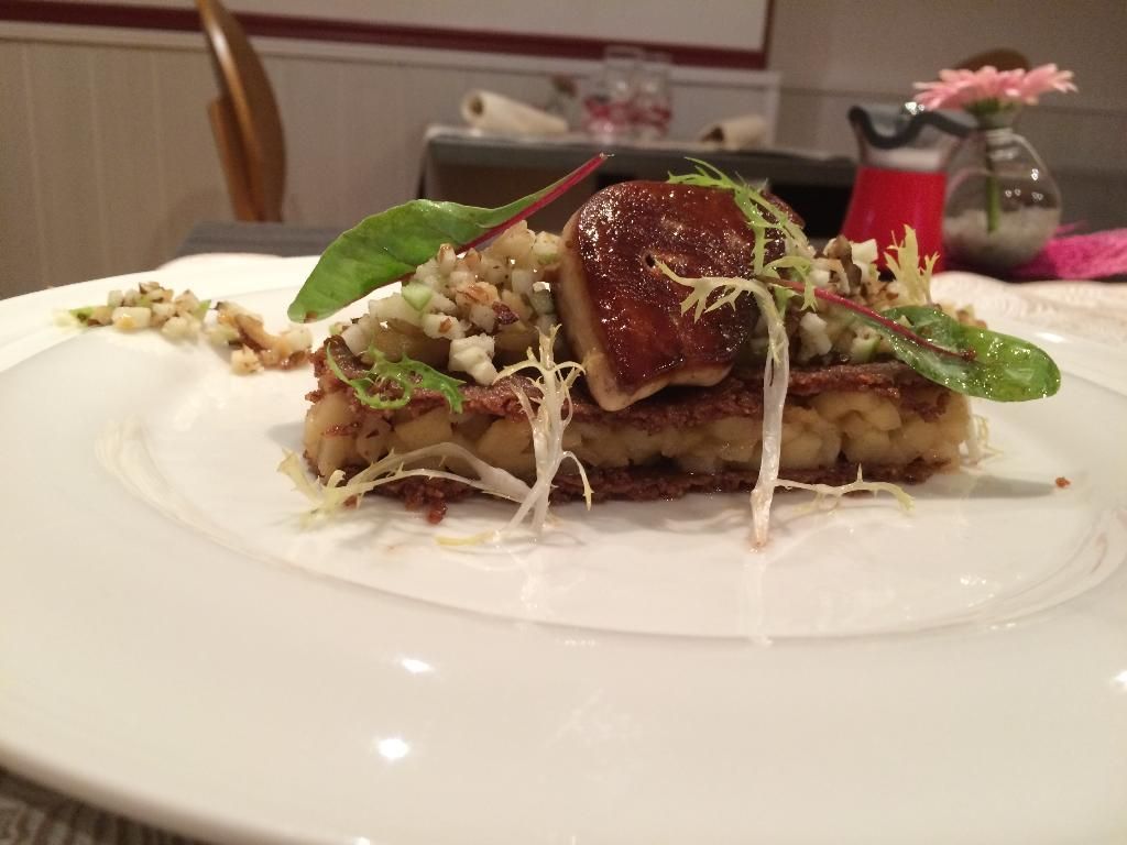 Assiette gourmande composée de foie gras poêlé, de légumes verts et d'une garniture sur une galette de pommes de terre, le tout présenté sur une assiette blanche.