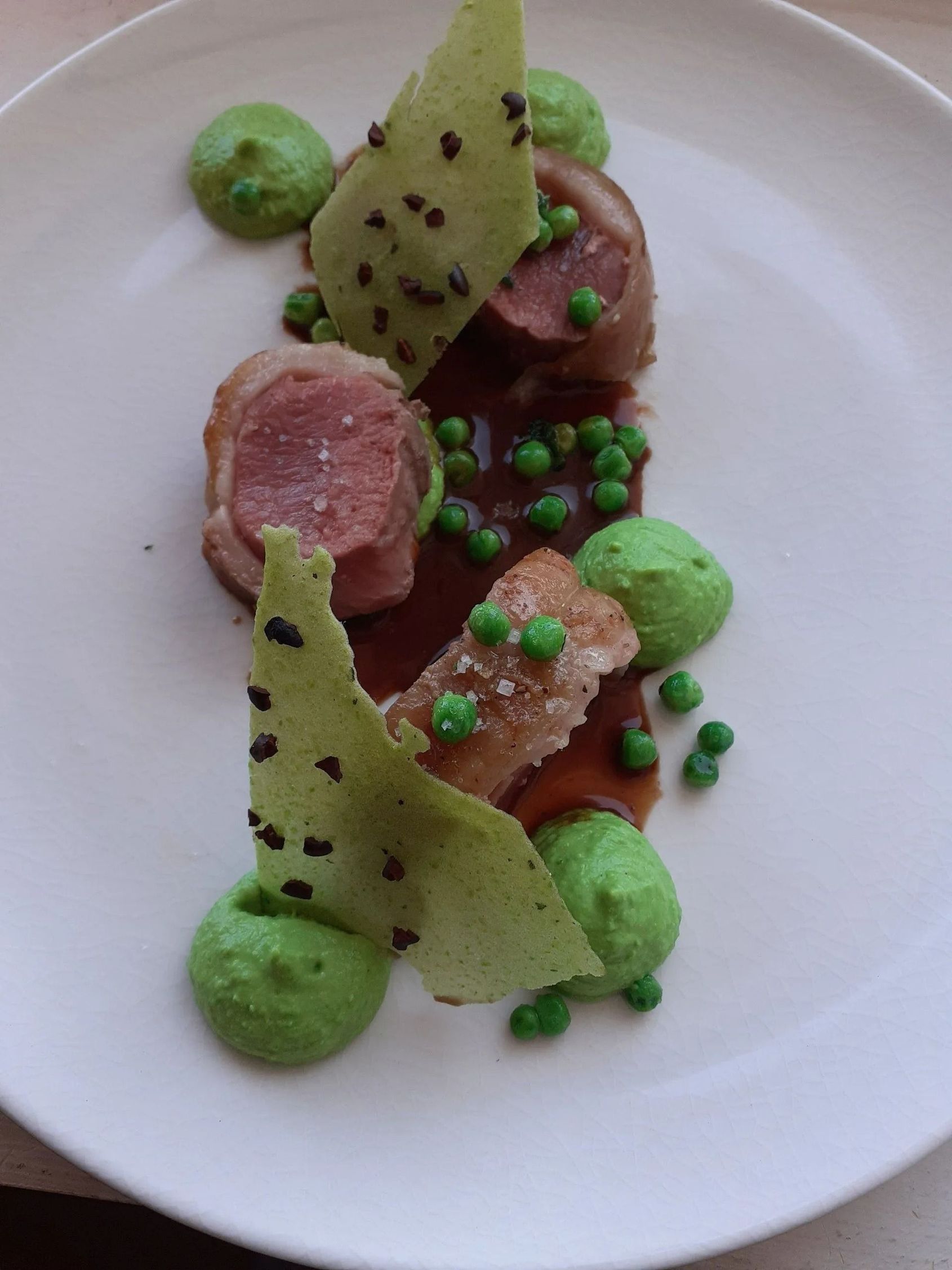 Assiette gourmande composée de viande enroulée de bacon, de purée de petits pois, de frites vertes croustillantes et d'une sauce brune.