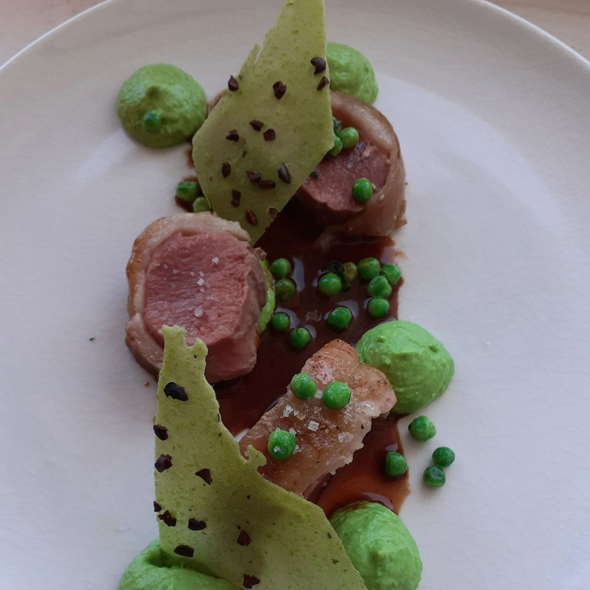 Assiette raffinée : rouleaux de viande accompagnés de purée, de petits pois et de chips vertes.