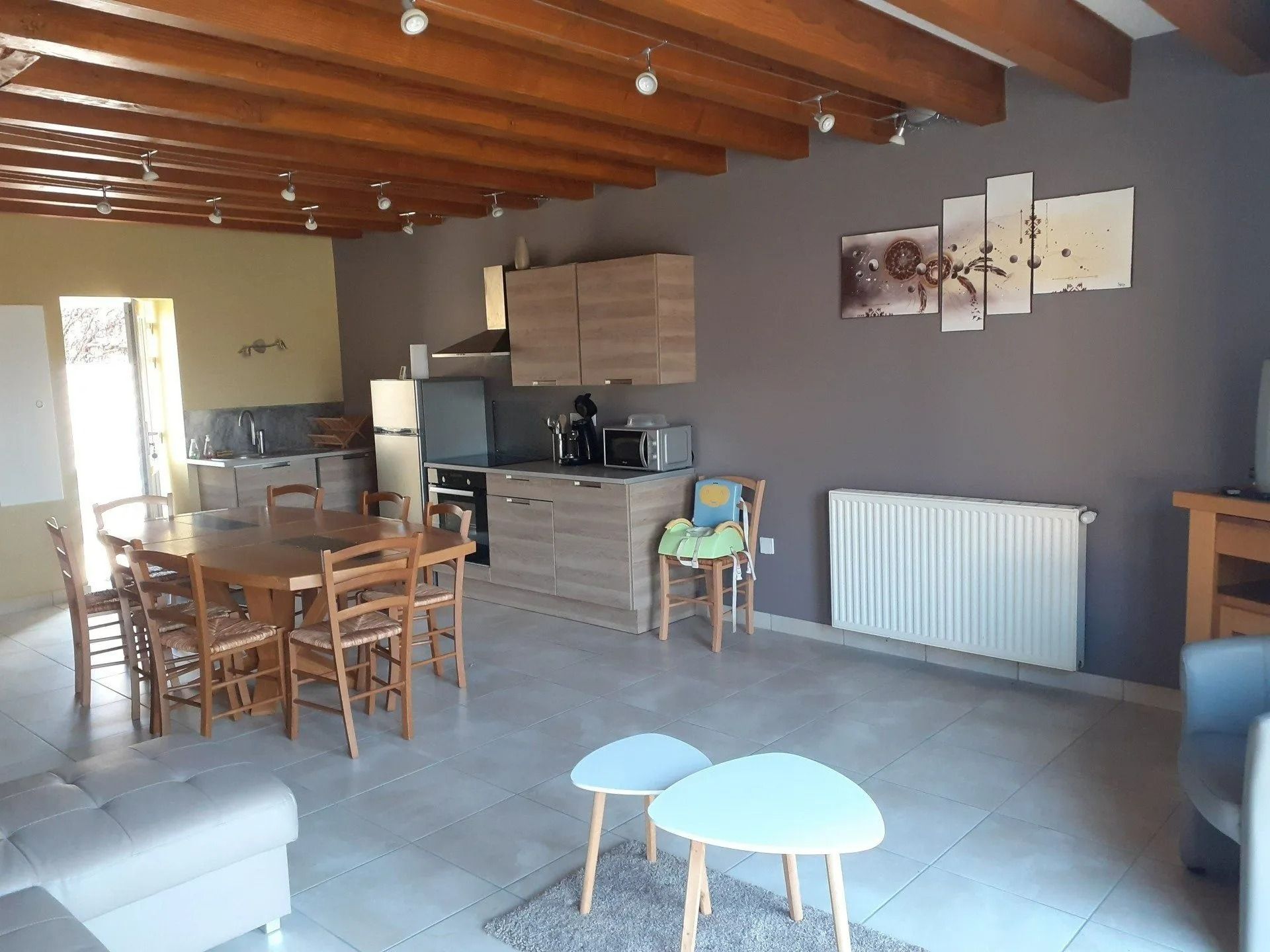 Cuisine et salle à manger ouvertes avec poutres apparentes, murs gris et meubles en bois.