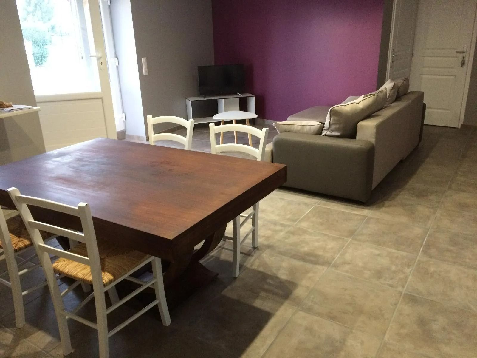 Salon avec table à manger et chaises, canapé gris, mur violet.