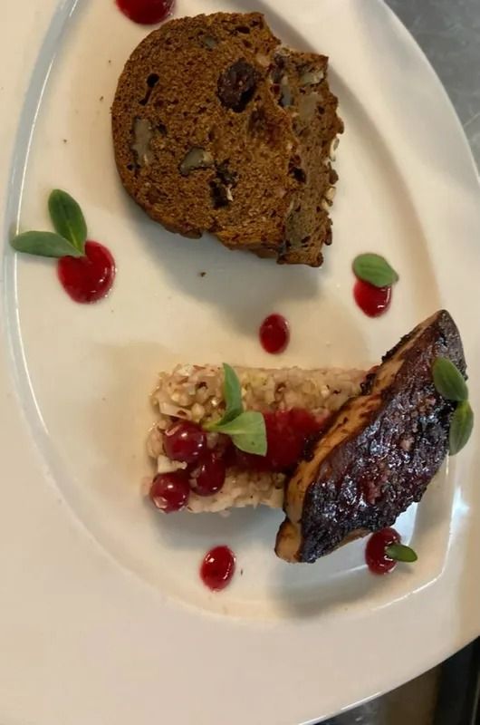 Dessert à l'assiette : gâteau aux noix, préparation rectangulaire de céréales et de baies, et aliments foncés poêlés ; points de sauce rouge et feuilles vertes.