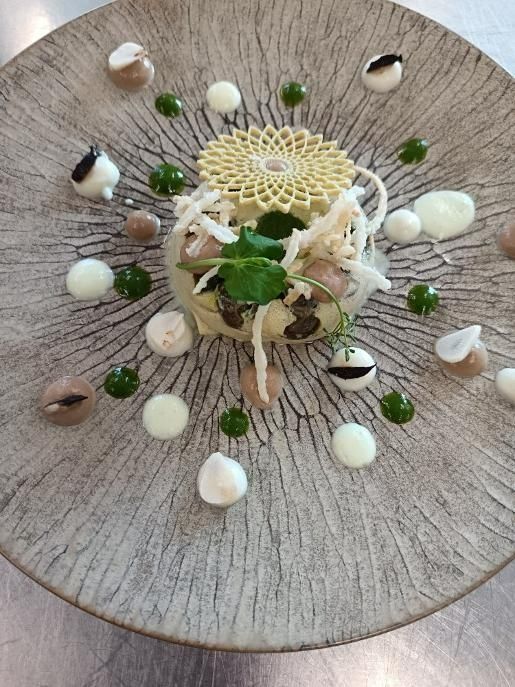 Présentation gastronomique sur une assiette grise texturée : une composition de légumes centrale entourée de sauces et d’éléments décoratifs.