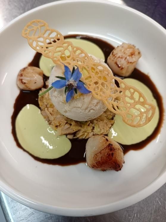 Noix de Saint-Jacques poêlées, sauce, purée et garniture de biscuit sur une assiette blanche ; un plat raffiné.