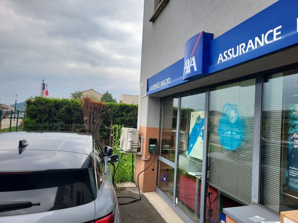 Bureau d'assurance en bord de rue avec une enseigne bleue ASSURANCE et une voiture garée à côté du bâtiment