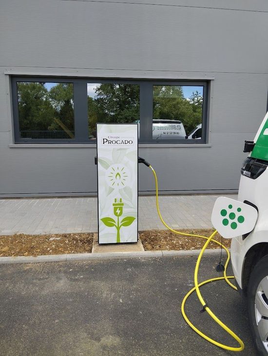 Borne de recharge pour véhicules électriques à côté d'un bâtiment gris, avec un câble jaune relié à un socle de recharge blanc.