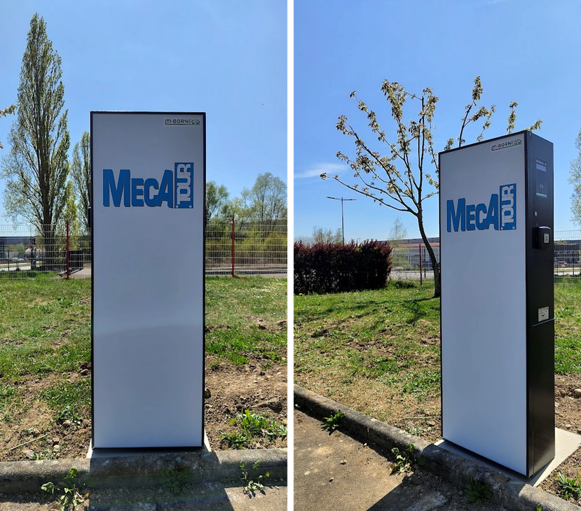 Kiosque Meca blanc avec logo bleu, vu de face et de côté, sur un terrain extérieur herbeux.