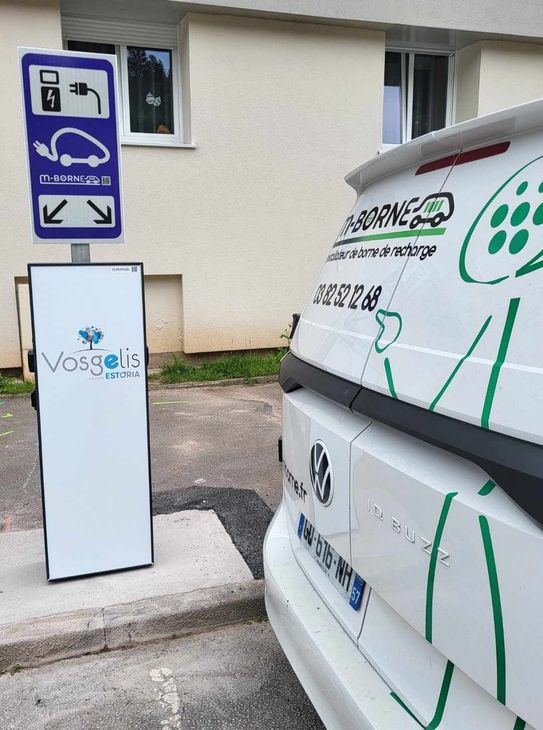 Borne de recharge pour véhicules électriques à côté d'une camionnette blanche avec des graphismes verts dans une aire de stationnement