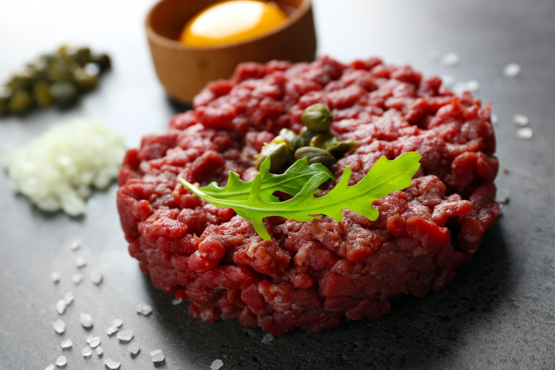 Tartare de bœuf haché cru garni de persil, de sel et de condiments sur une surface foncée