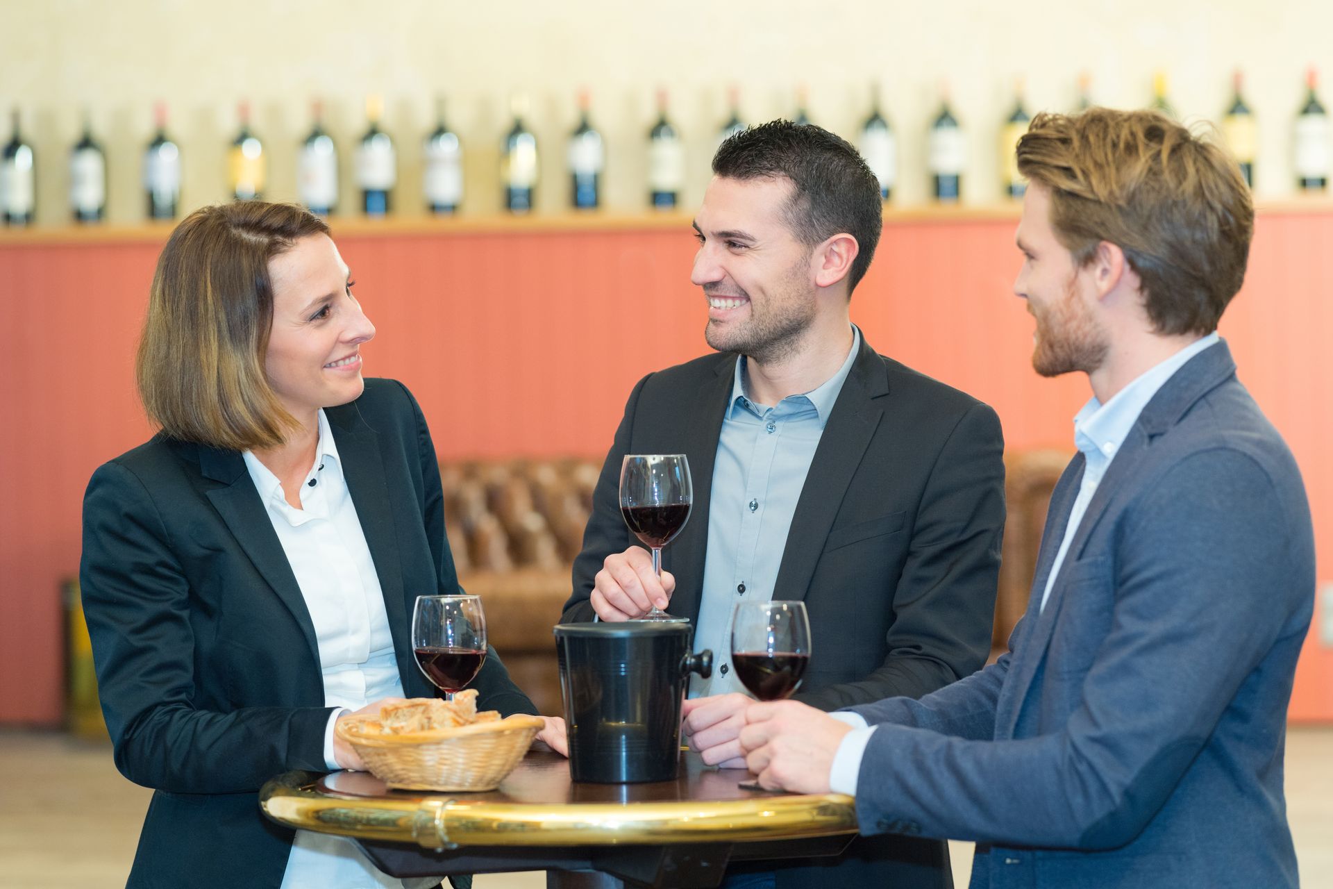 Trois collègues discutent à une table de bar, un verre à la main et du pain posé sur la table