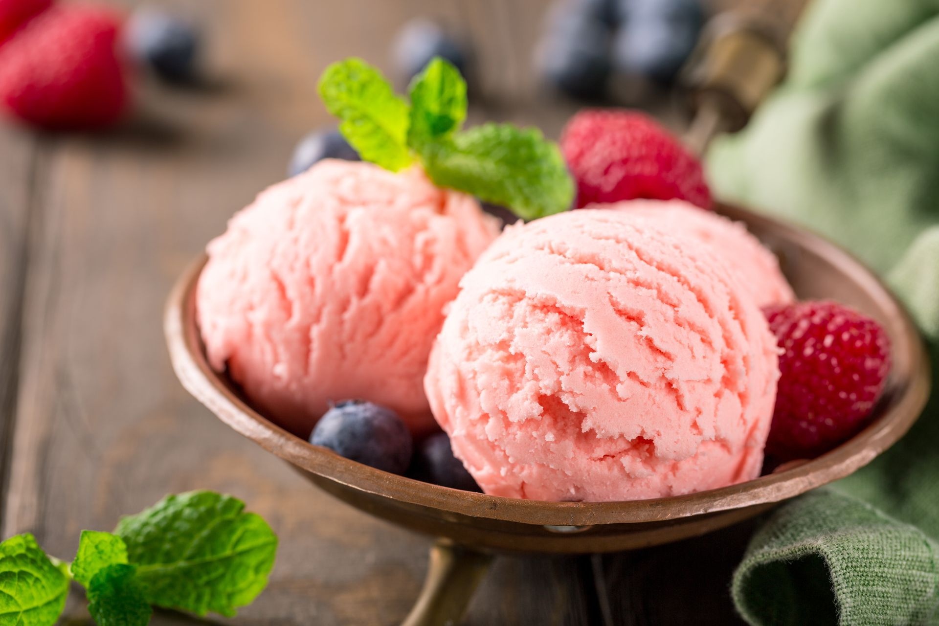 Deux boules de glace rose dans un bol avec des framboises, des myrtilles et des feuilles de menthe