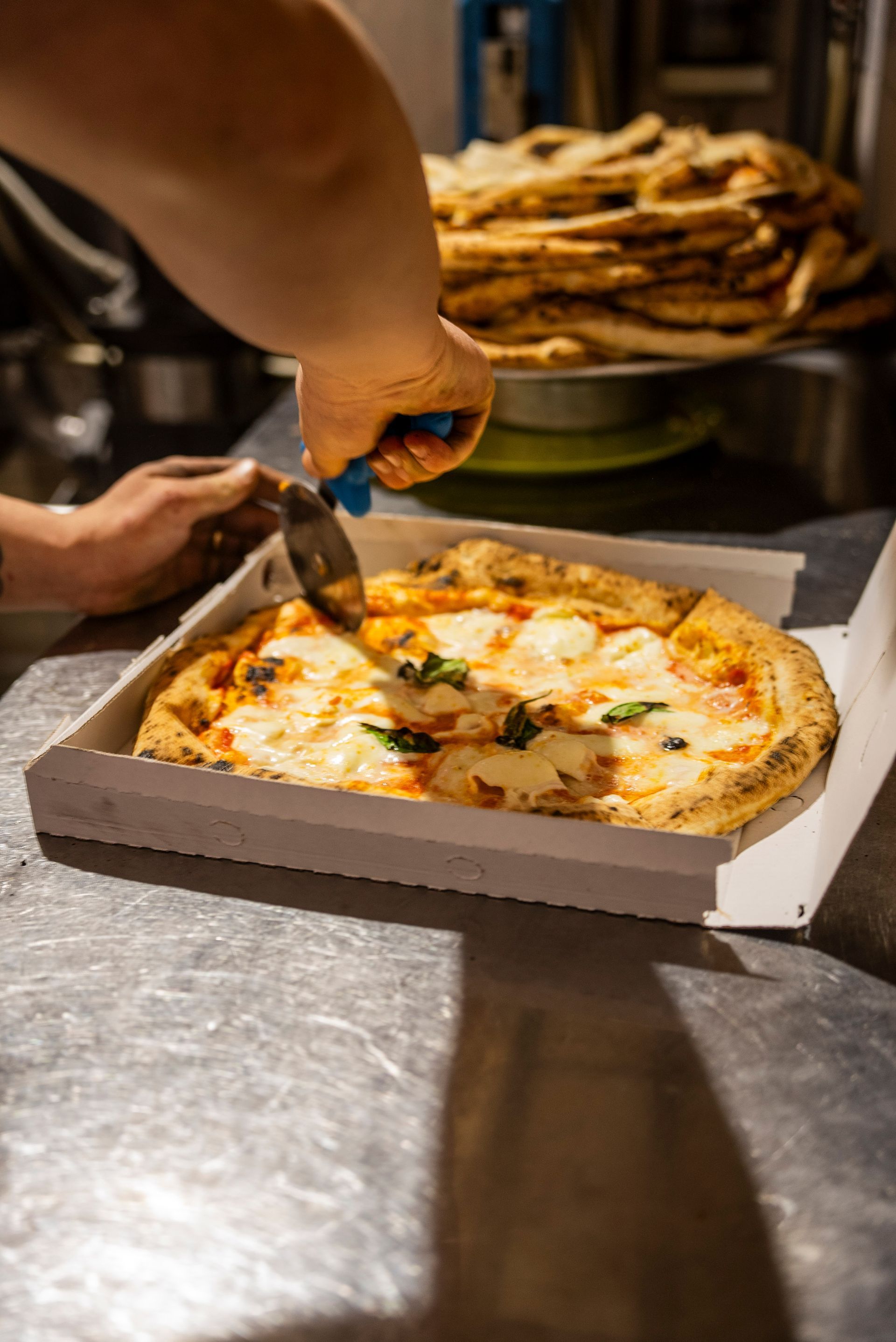 Une main découpant une part sur une pizza fraîchement cuite dans la cuisine d'un restaurant