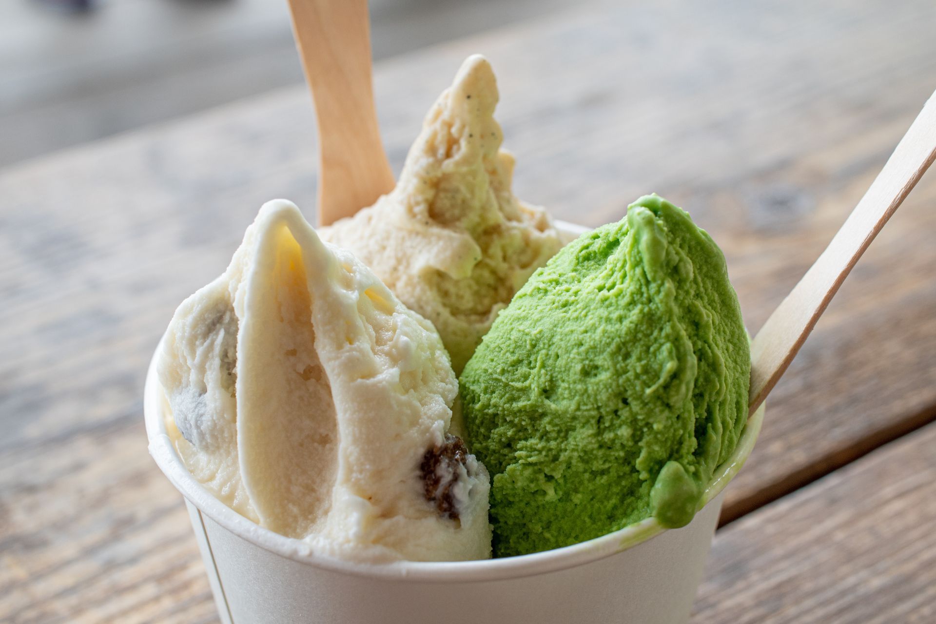Trois boules de glace disposées dans une coupe sur une table en bois avec des cuillères
