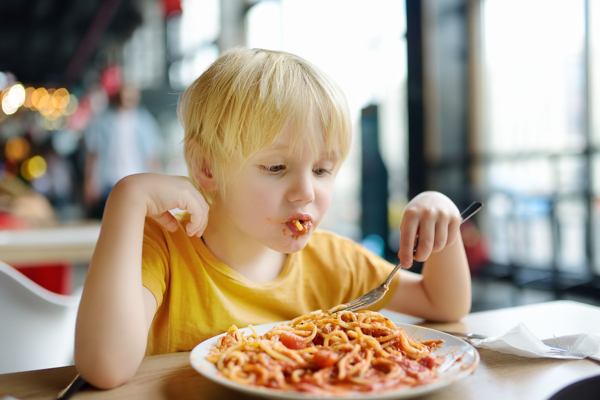 Enfant en chemise jaune mangeant des spaghettis à la table d'un restaurant