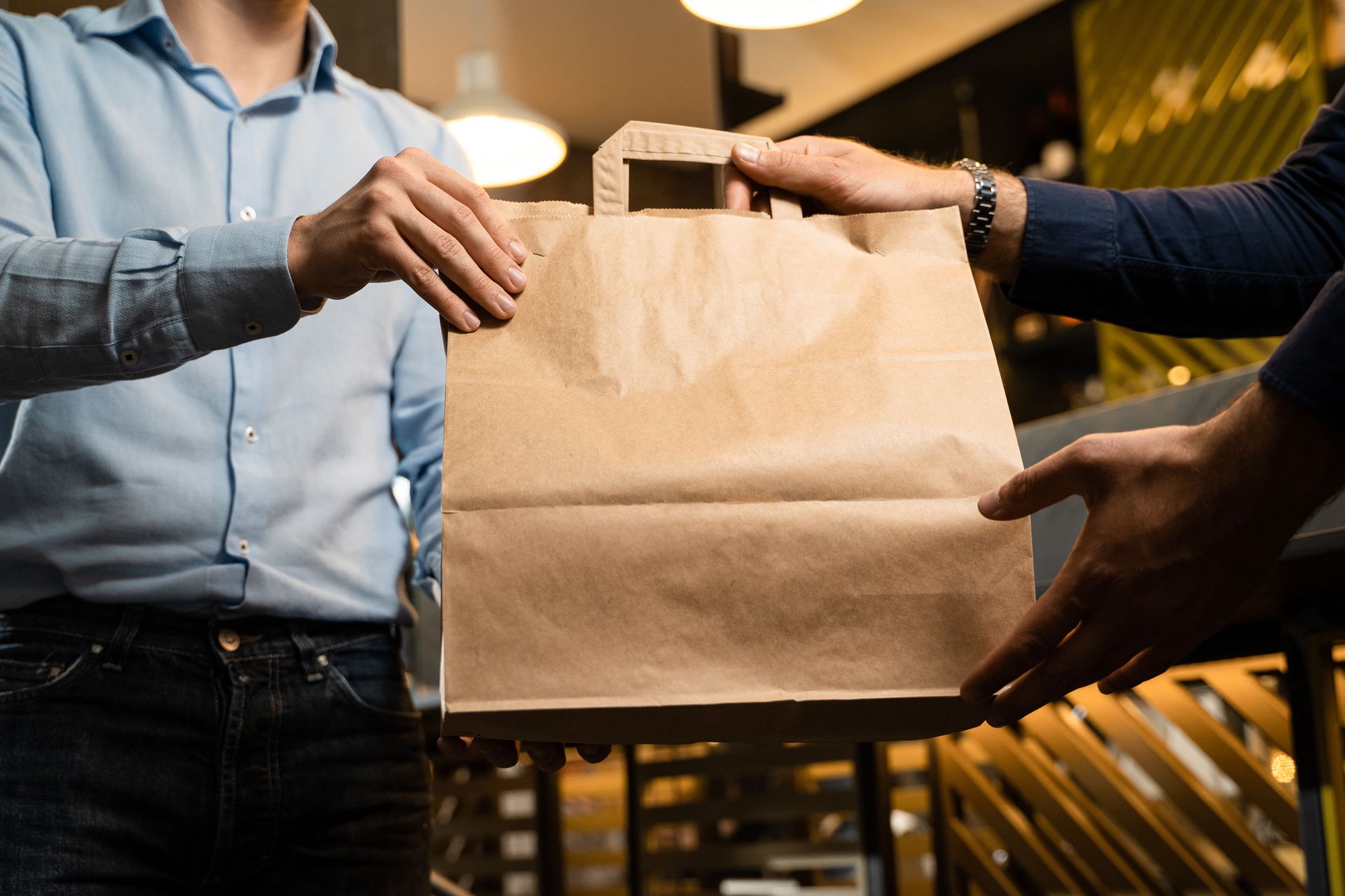 Deux personnes échangent un sac en papier brun dans un restaurant à l'éclairage chaleureux