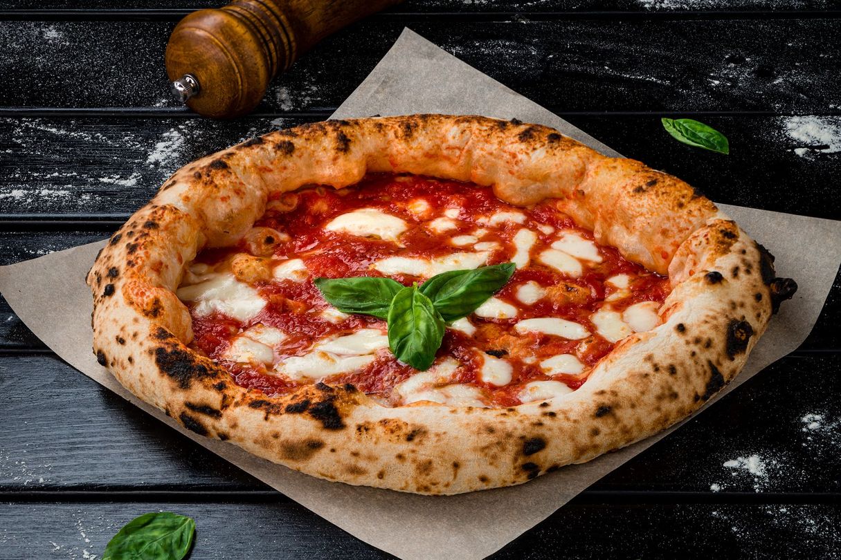 Pizza Margherita cuite au feu de bois sur papier sulfurisé avec du basilic, sur une table en bois foncé