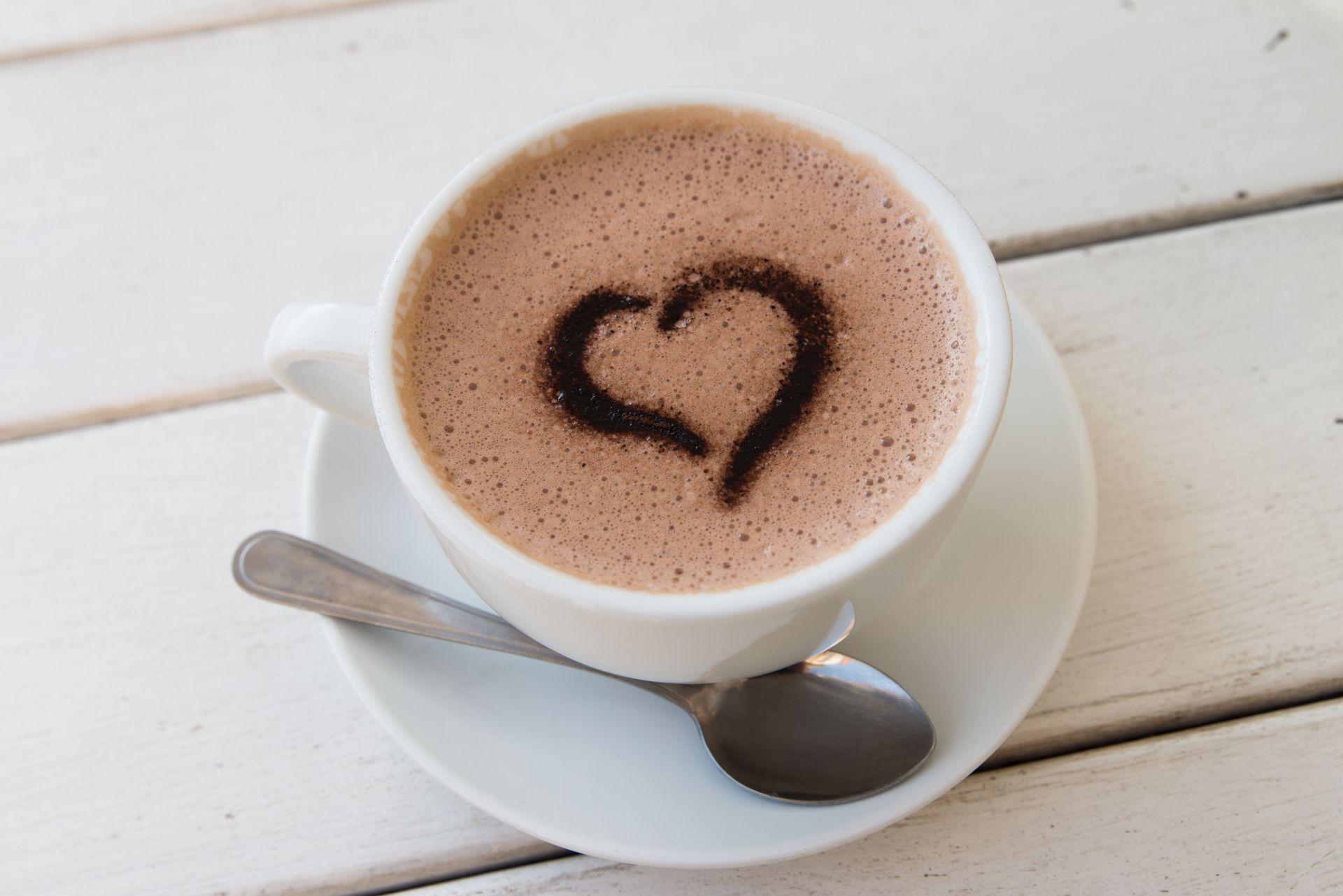 Tasse de café avec une mousse en forme de cœur, servie sur une soucoupe blanche avec une cuillère